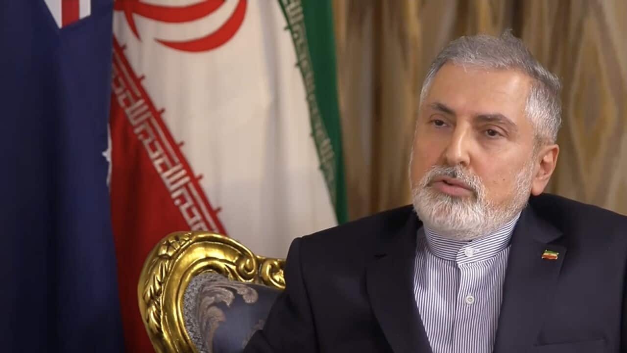 A man sitting on a chair, behind Australian and Iranian flags.