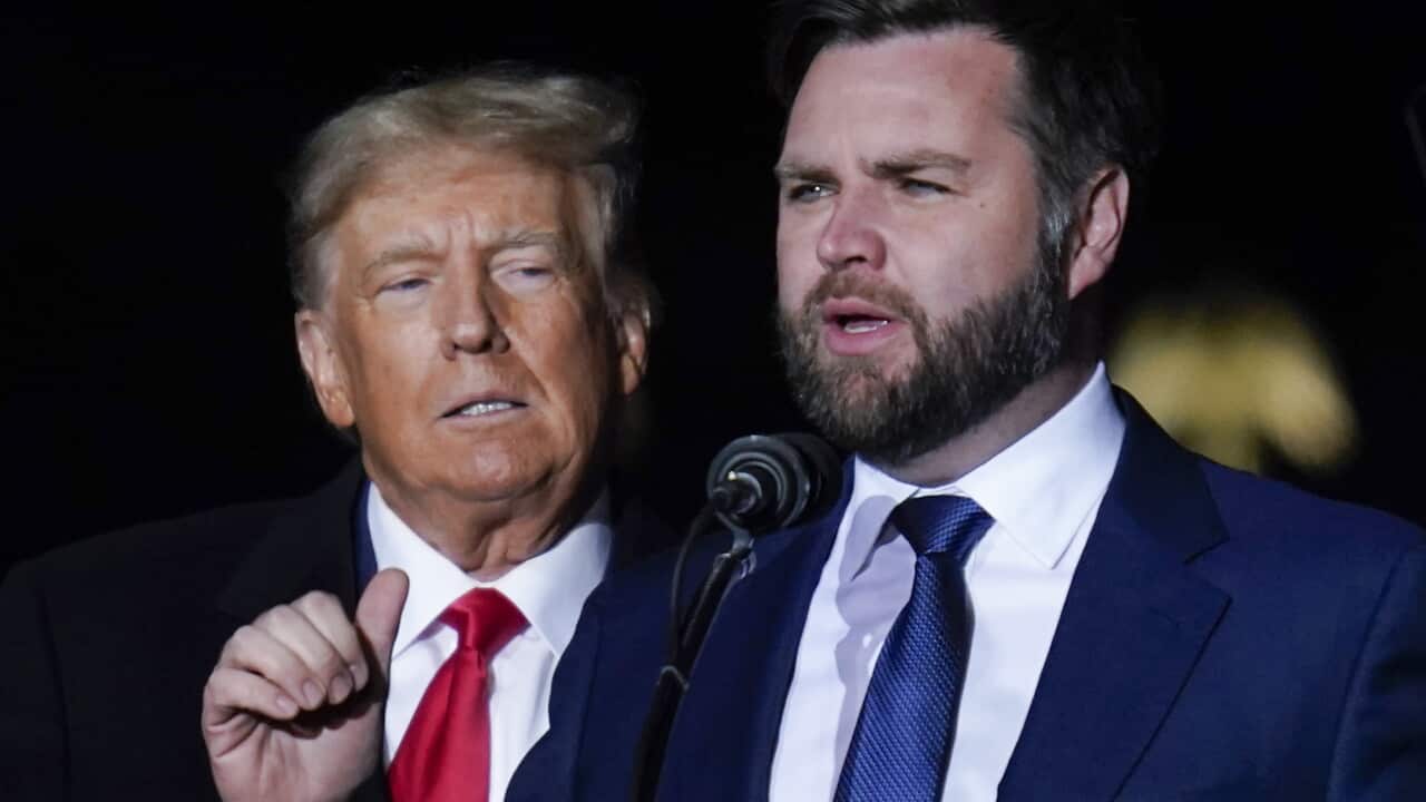 J.D. Vance speaking to a microphone with Donald Trump behind him.
