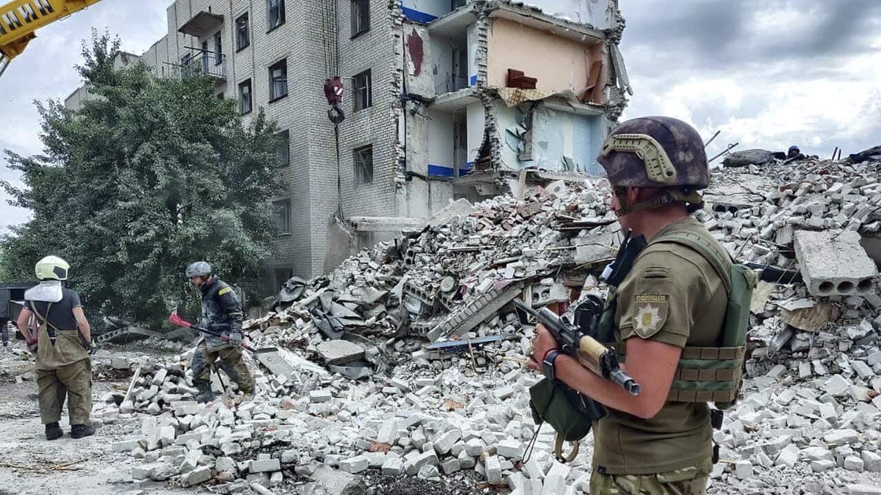 Ukrainian rescuers clean the debris around a destroyed building.