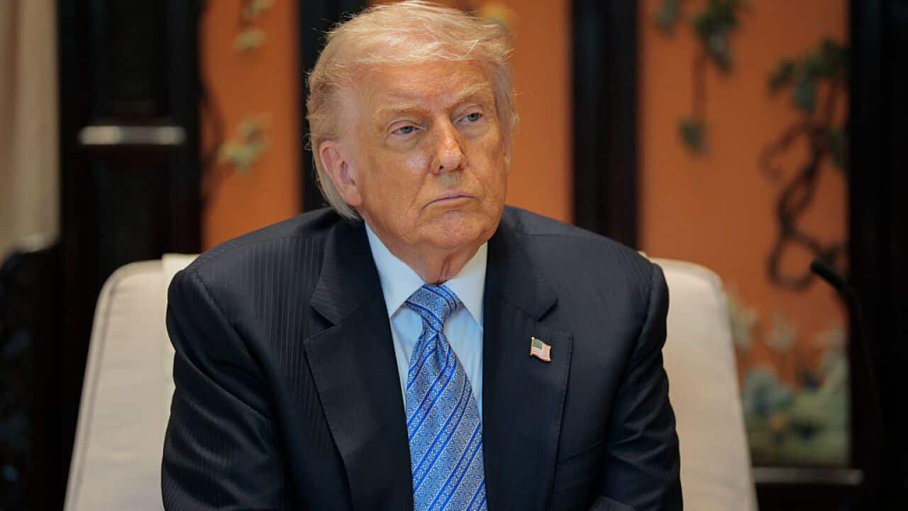 US President Donald Trump sits in a suit with a serious expression on his face.