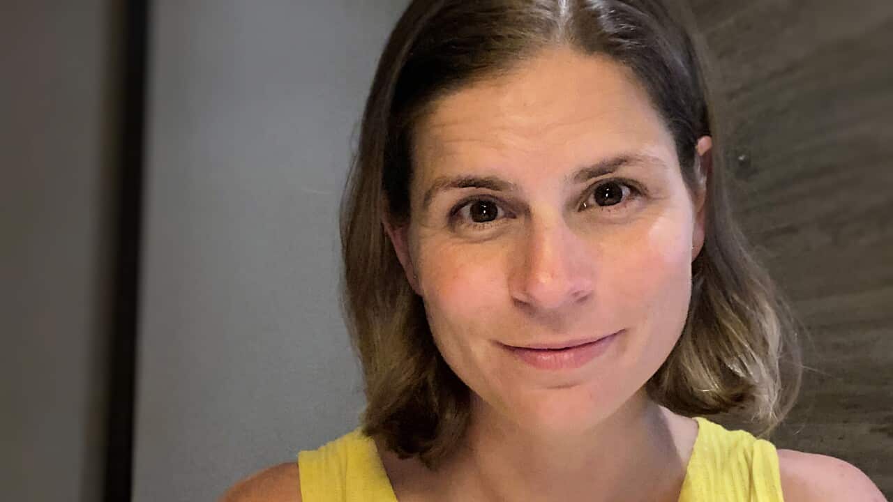 A woman in a yellow top with a slight smile looks at the camera.