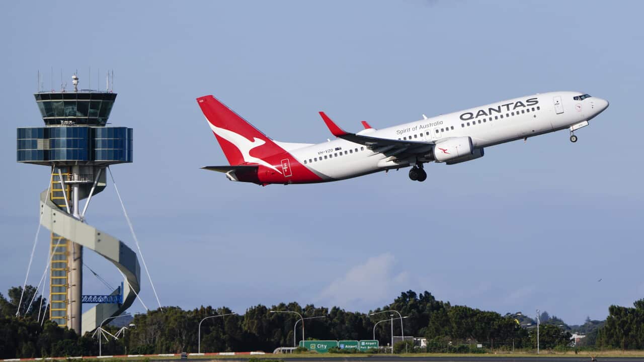 A red and white plane takes off at an airport. An air traffic control tower is seen in the background