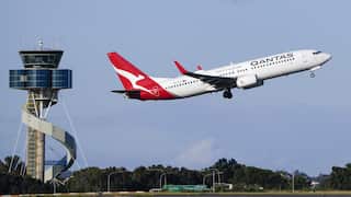 A red and white plane takes off at an airport. An air traffic control tower is seen in the background