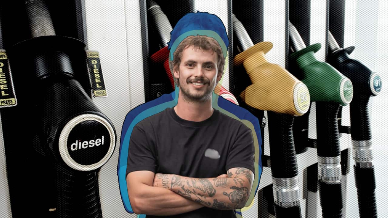 A man smiling and crossing his arms. He is against a background of a petrol pump.