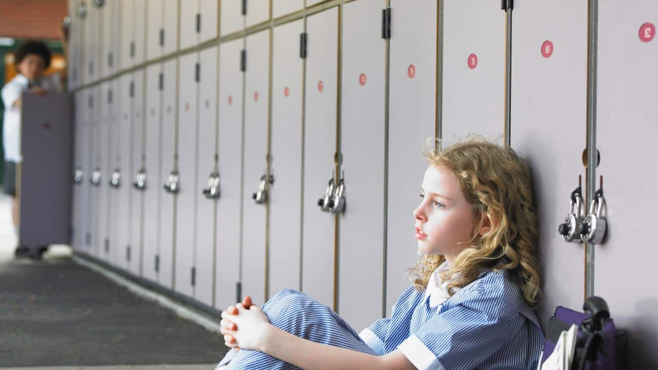 Elementary schoolgirl sitting on floor against school lockers
