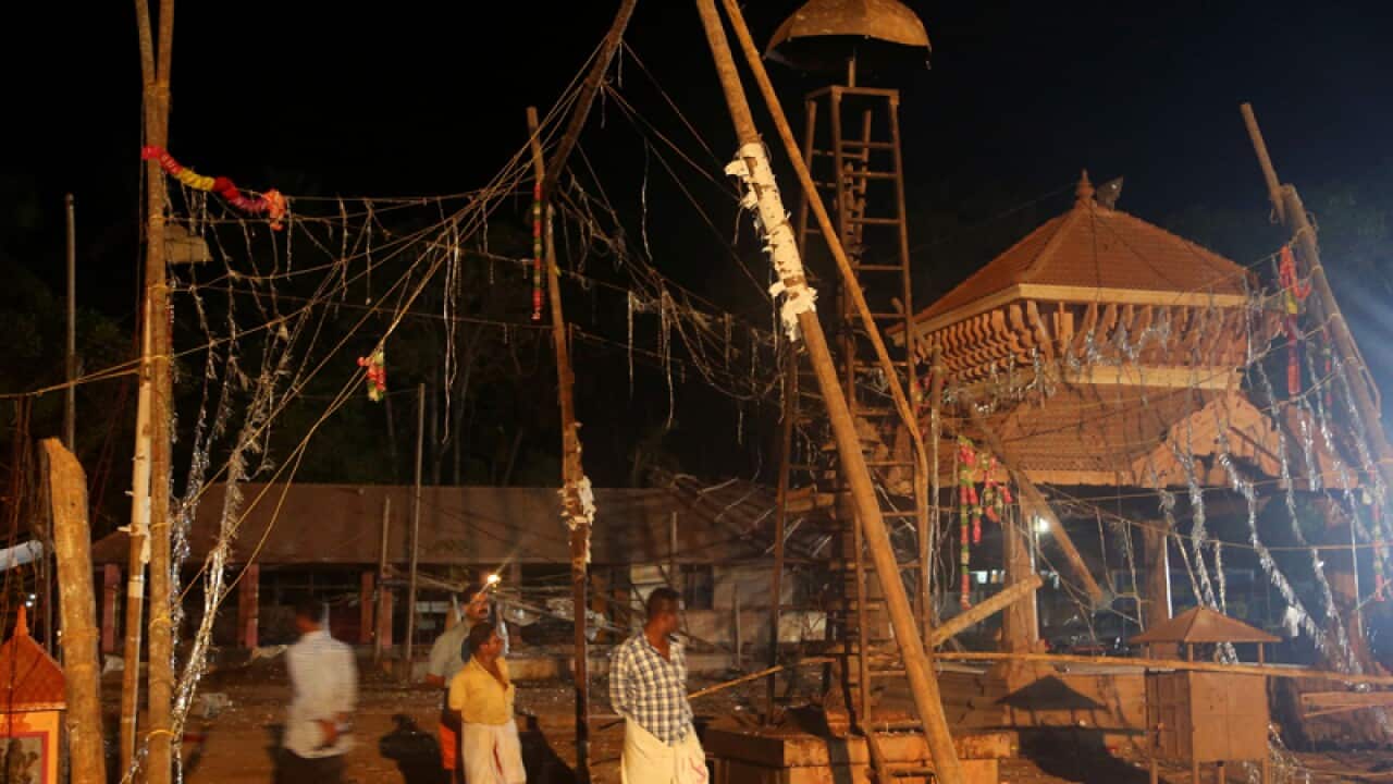 People walk past damaged structures at the Puttingal temple complex