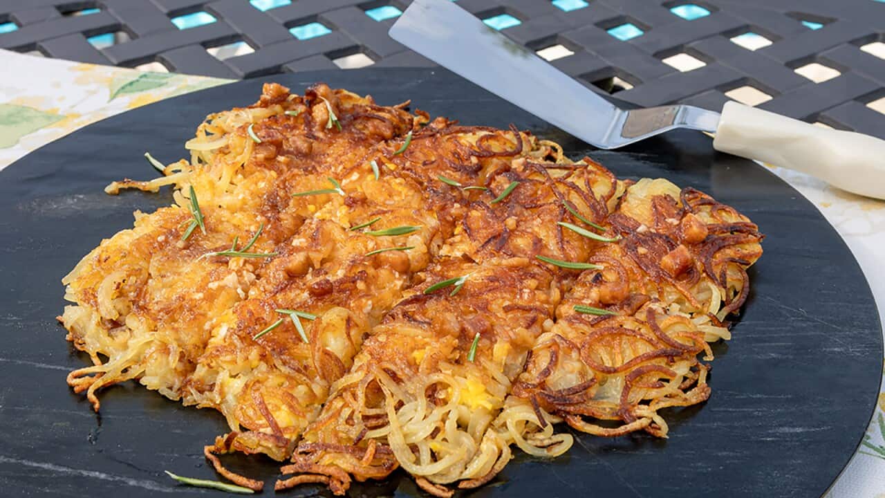 A golden-brown crisp-looking layer of spiralised potato rosti sits on a round black platter.