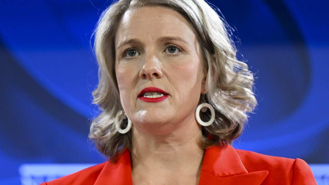A woman speaking into microphones while standing at a lectern.