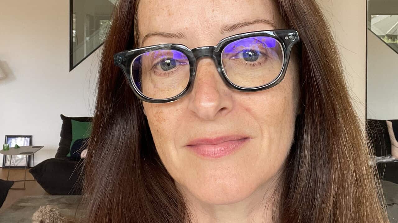 A selfie on a woman in long brown hair and glasses. She has a neutral expression on her face.