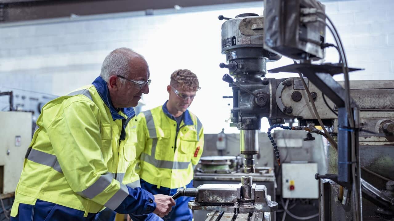 Engineer mentoring apprentice on traditional lathe in engineering factory
