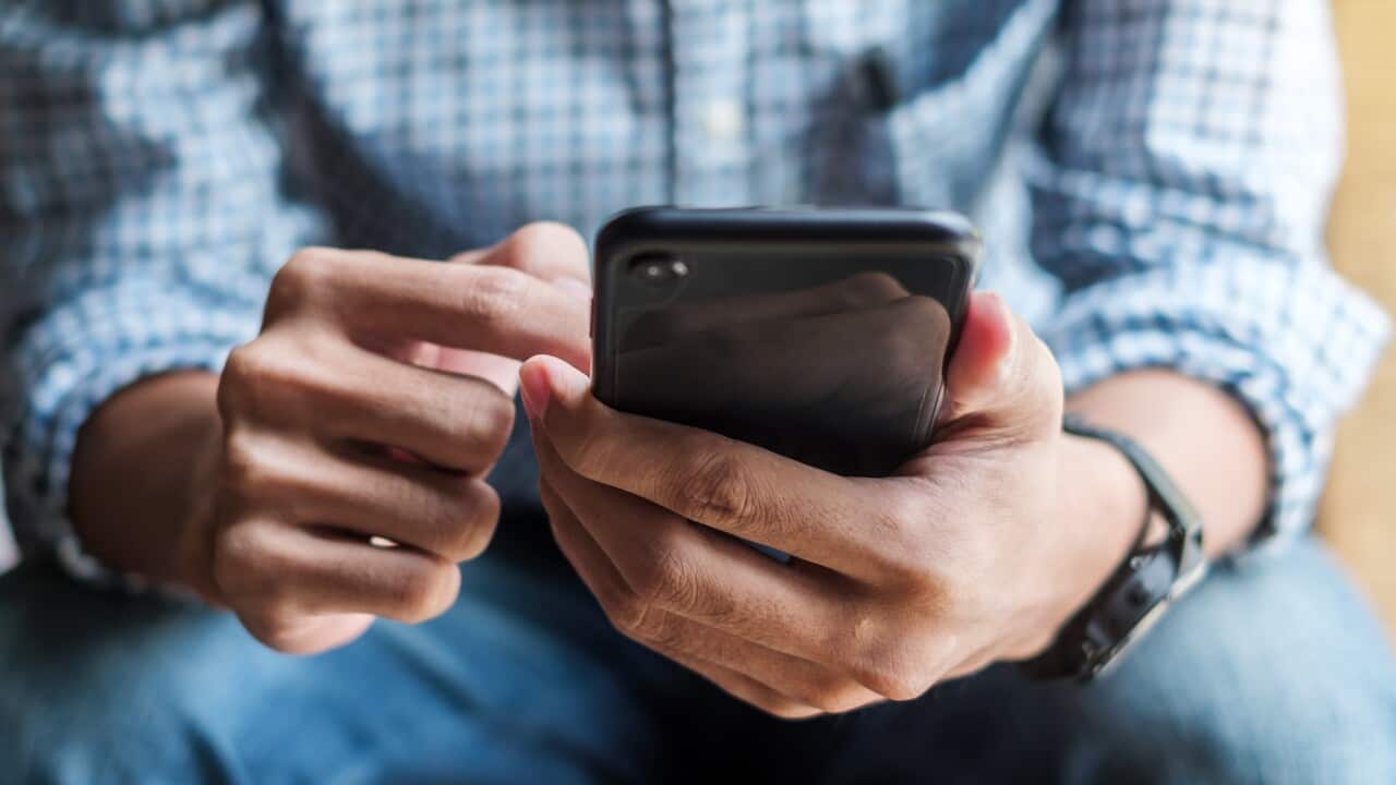A man sitting down with a mobile phone in his hand.