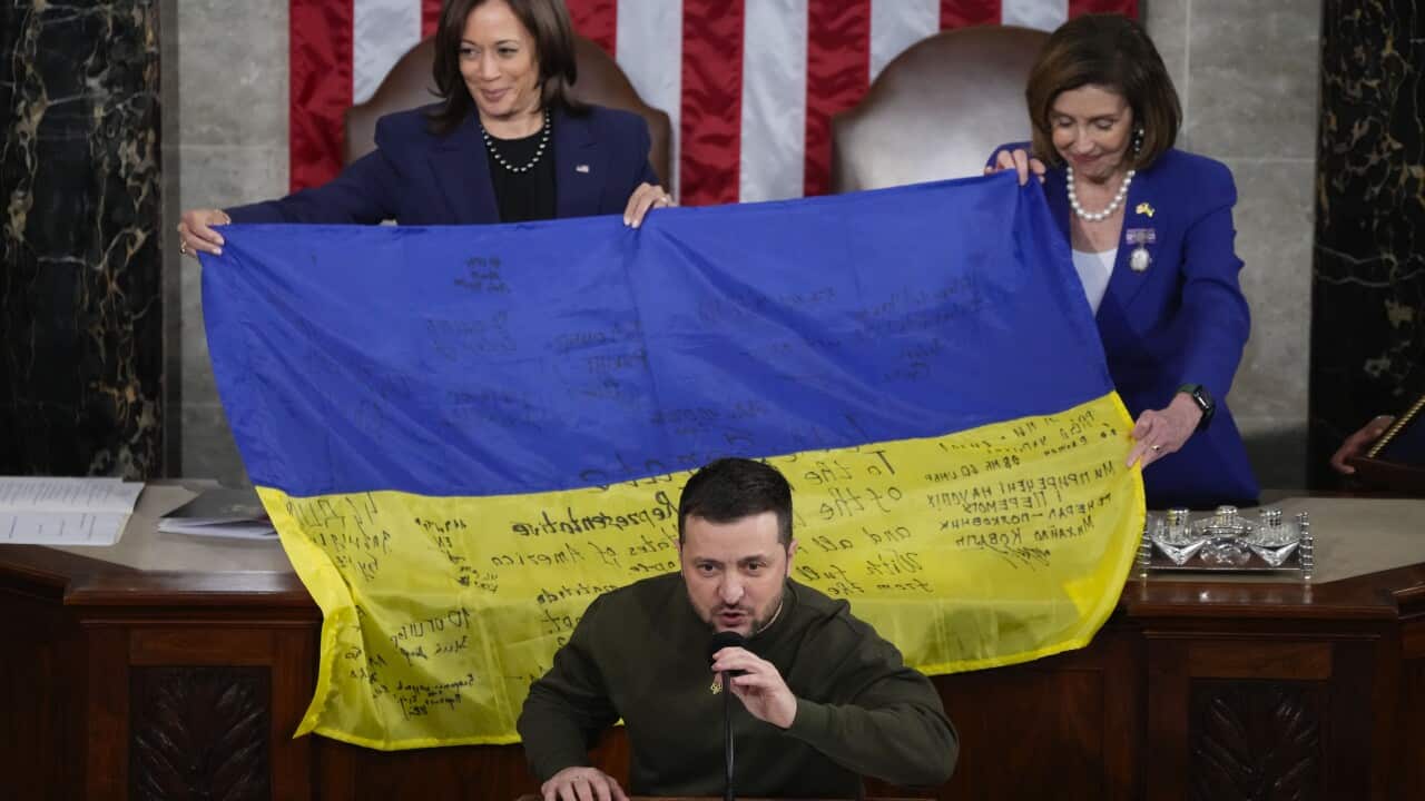 A man addresses leaders in the US as a Ukrainian flag is held by two women behind him.