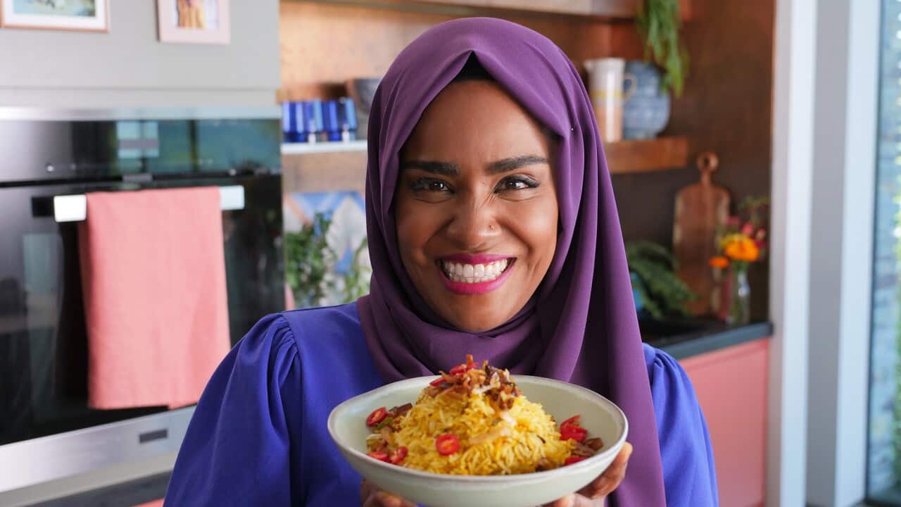 Nadiya stands in her kitchen, smiling, and holding a bowl biryani.