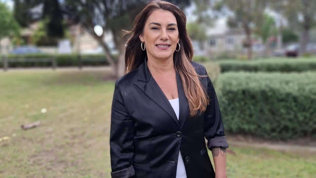 A woman in a black blazer and white shirt standing in front of a garden