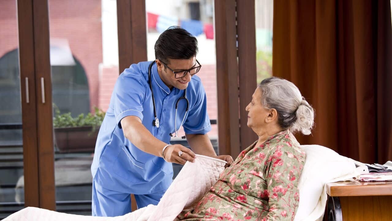 Male nurse home caregiver helping senior woman relaxing on bed