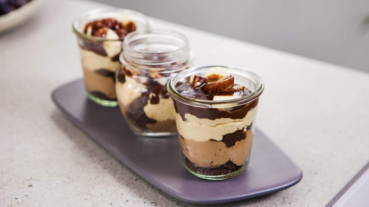 Three glass jars sit on a purple tray, each with layers of creamy, dark brown and light brown filling.