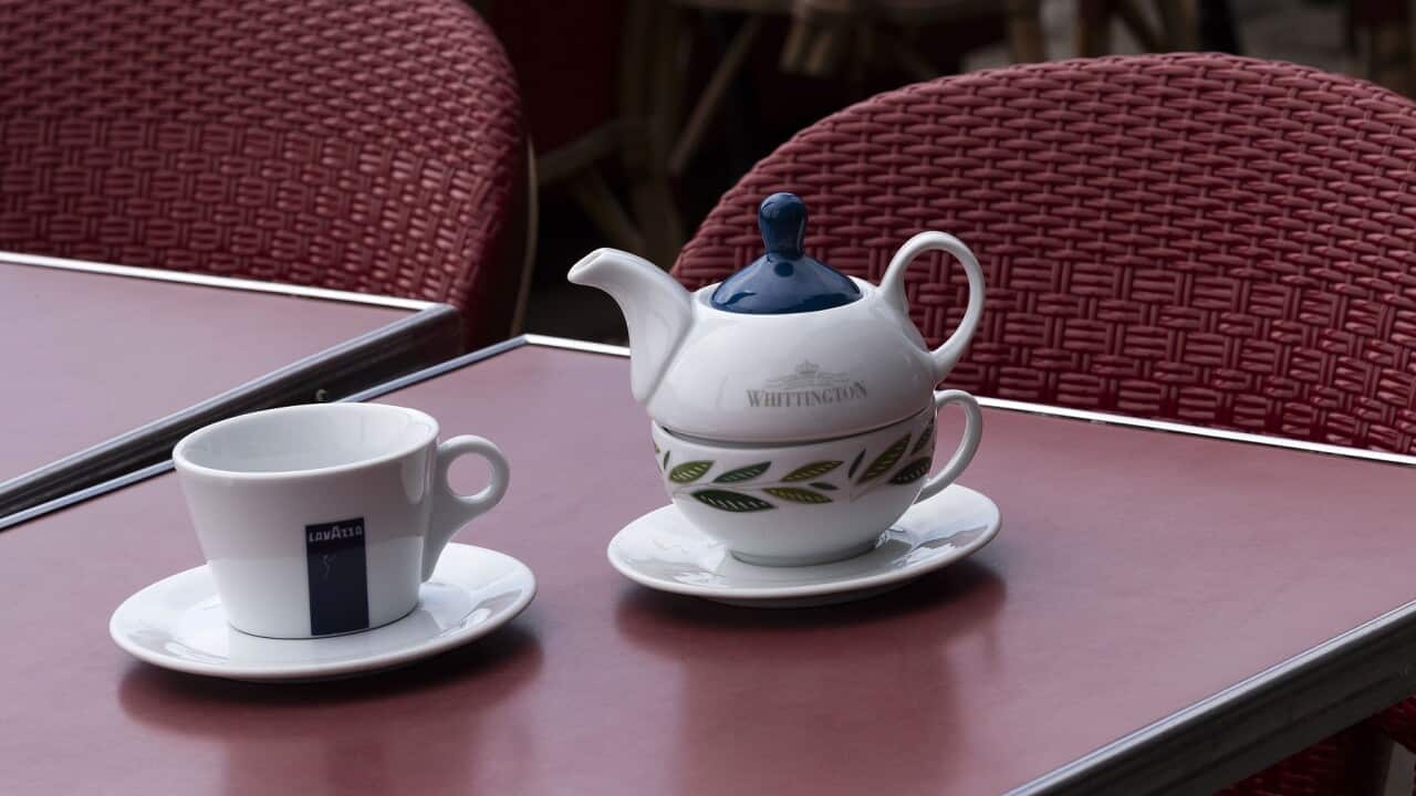 Tea cup and teapot with a coffee cup on a cafe table outside.