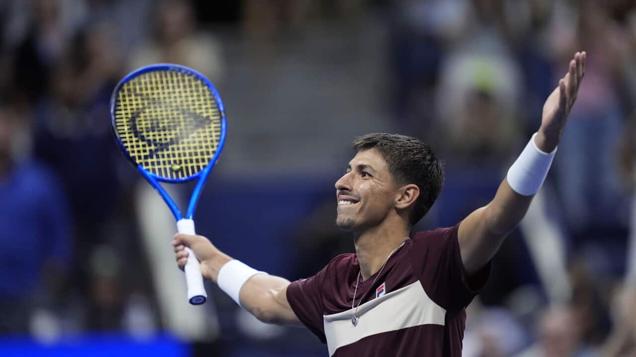 A male tennis player raises his hands and smiles at a crowd.