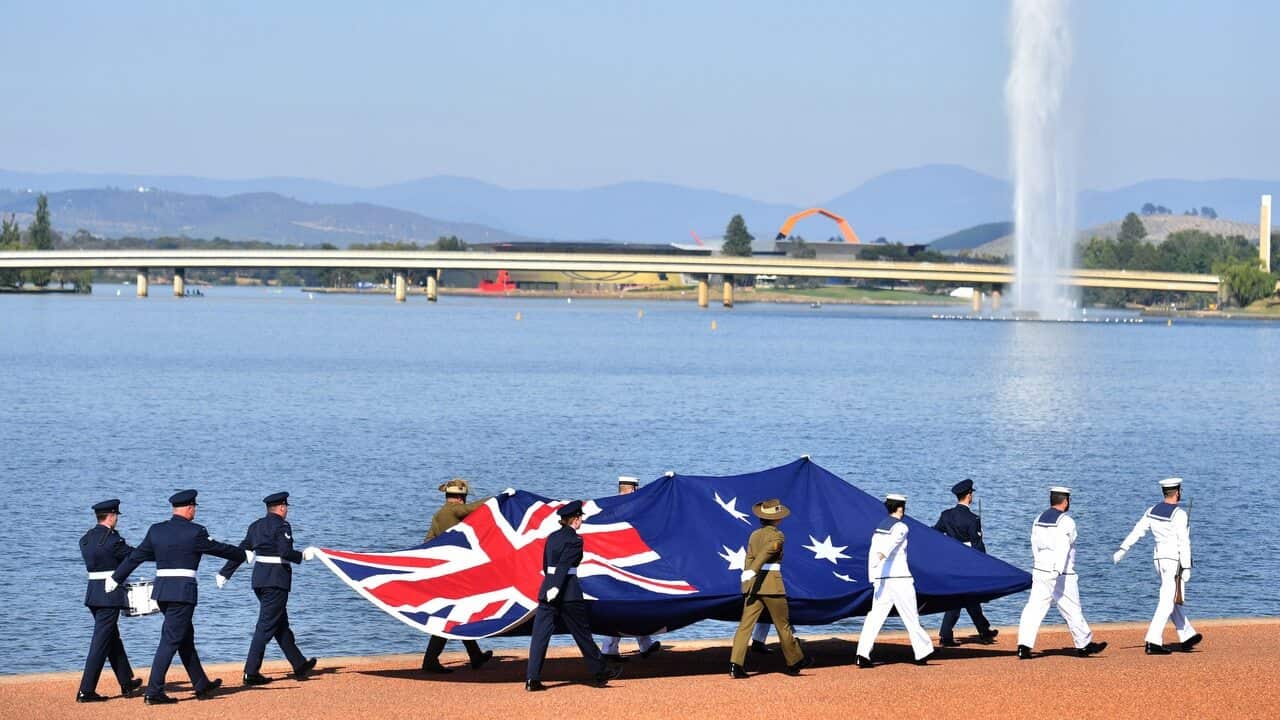 Defence personnel march past with the Australian flag at an Australia Day Citizenship Ceremony and Flag Raising event in Canberra.