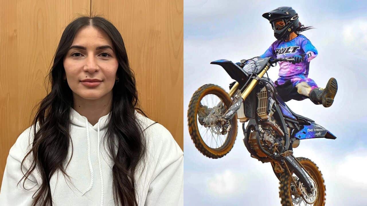 A closeup shot of a young woman with long brown hair in a white hoodie in front of a timber background