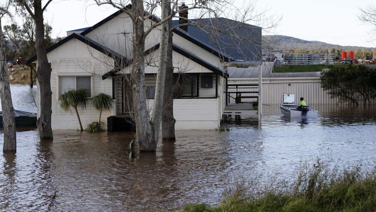 A man in a tinny next to a flooded house.