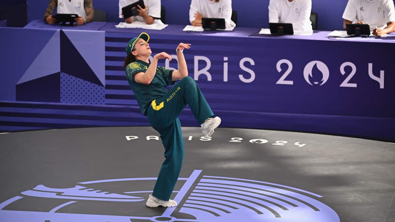 A woman wearing a green and gold sports uniform performs a dance move