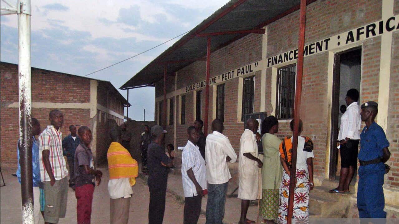 Abantu bahagaze k'umurongo imbere mu kurindira yuko binjira gutora