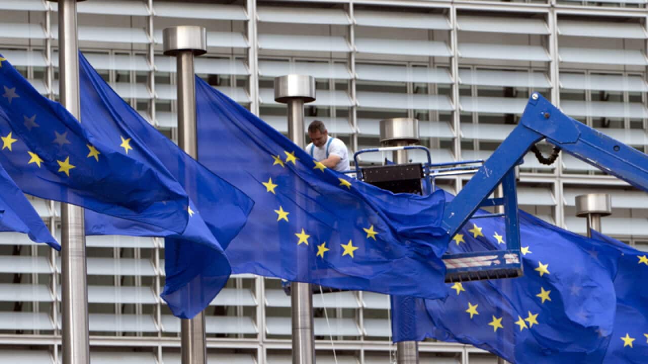 A worker on a lift adjusts the EU flags in front of EU headquarters