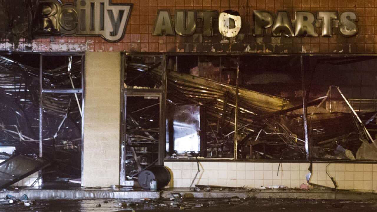 Police stand watch over the burned remains of an auto store