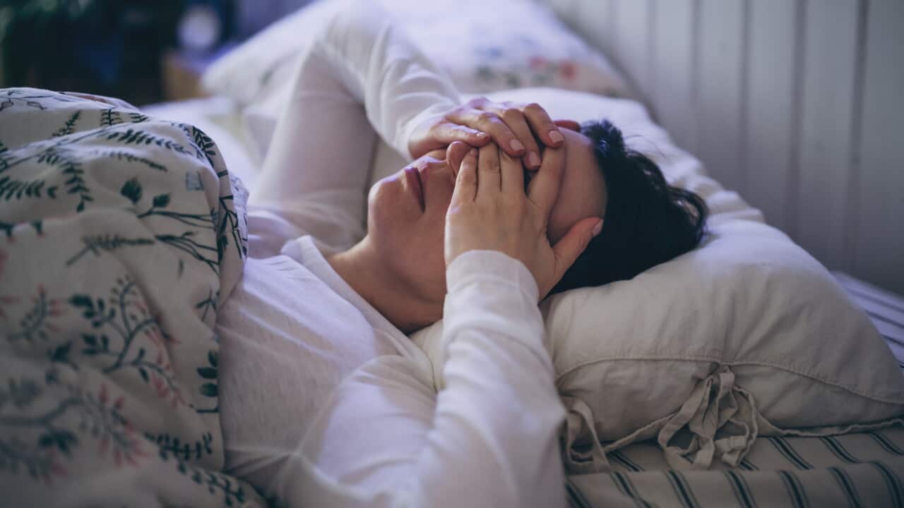 A person lying in a bed with their hands over their eyes.