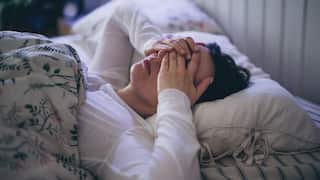 A person lying in a bed with their hands over their eyes.