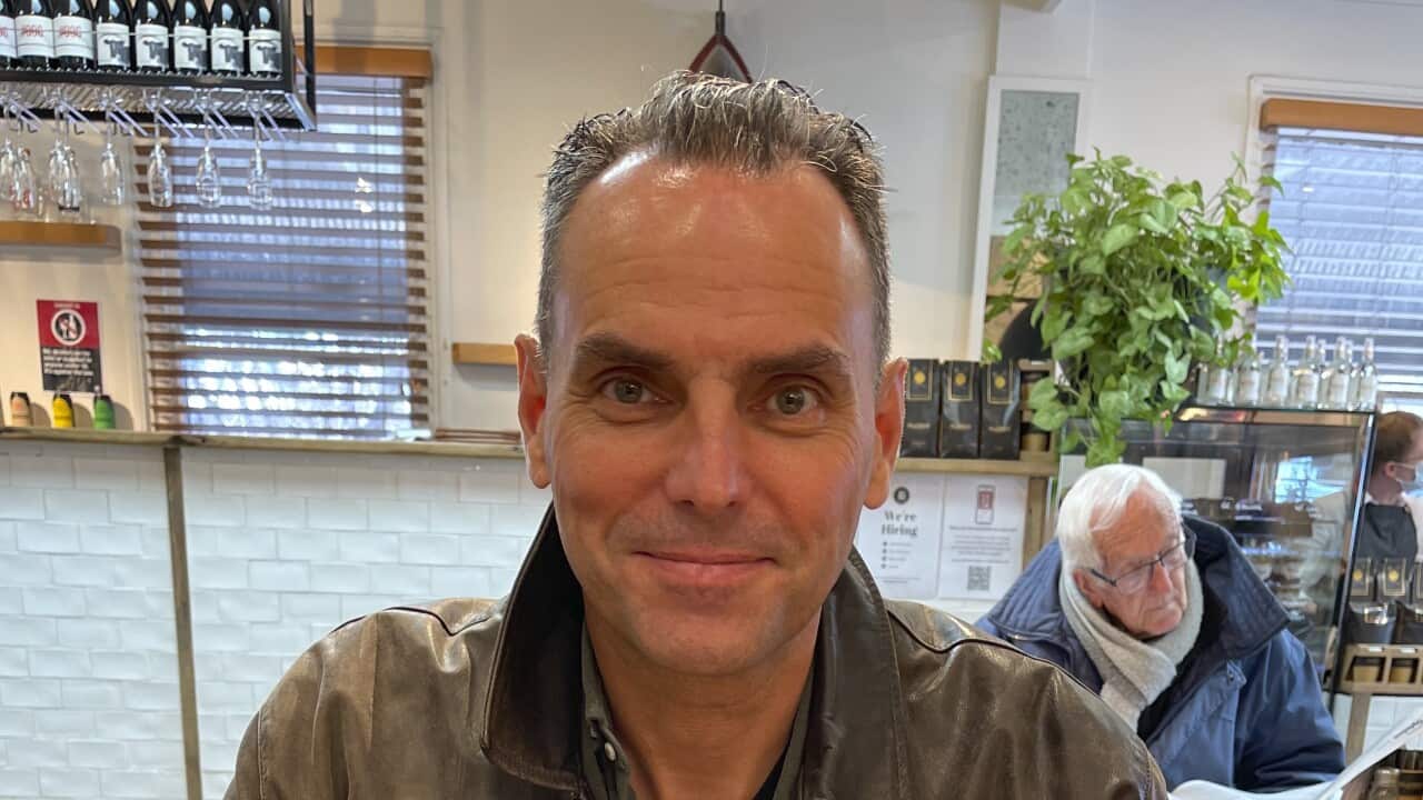 A man wearing a leather jacket smiles as he looks at the camera.