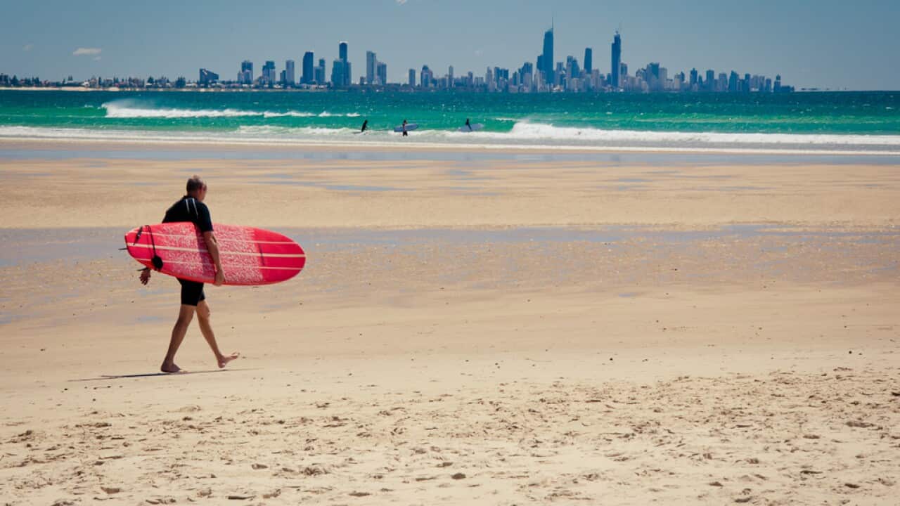 A surfer heading out at Currumbin beach with the Gold Coast skyline in the background