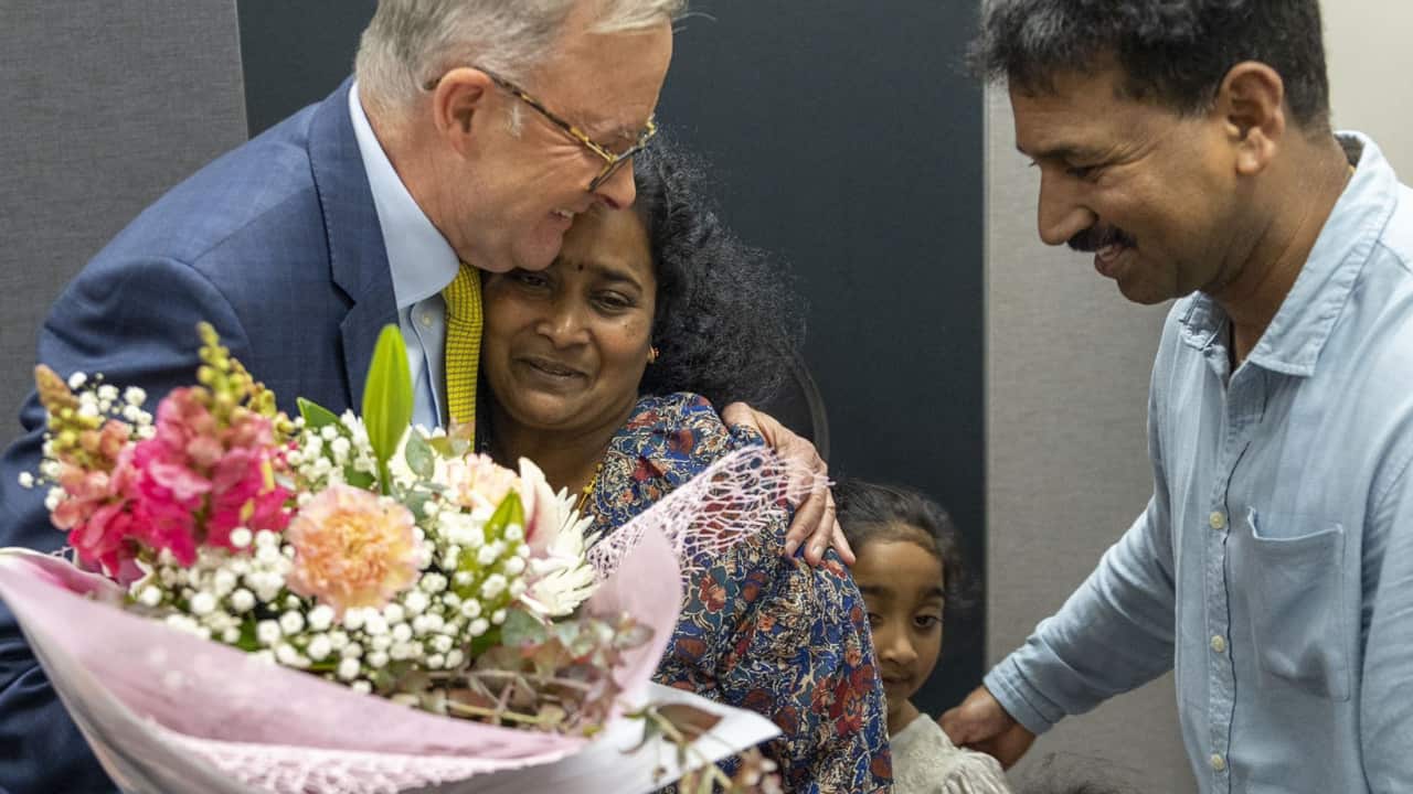 A man with his arm around a woman while her husband and two daughters look on.