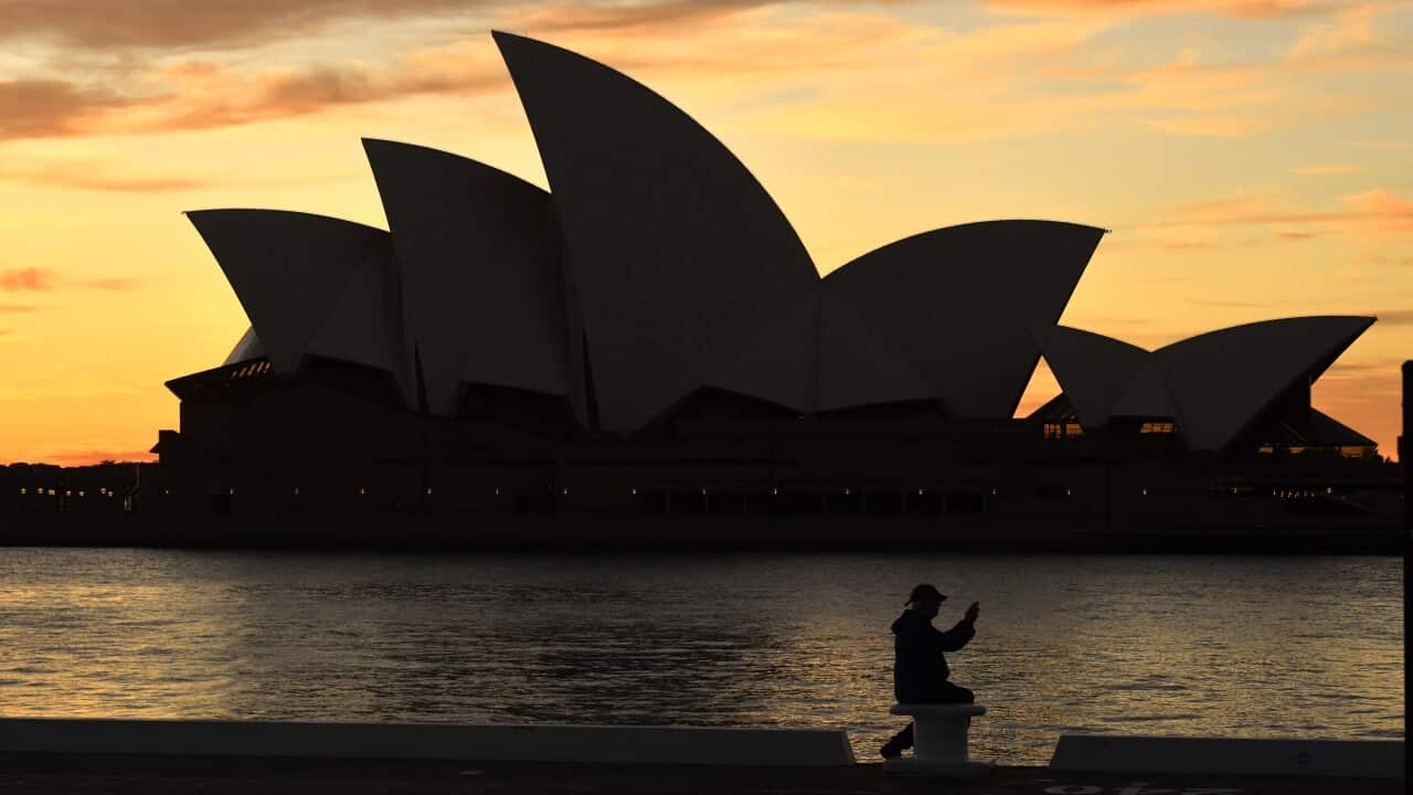 A man sits in front of the Sydney Opera House at dawn in Sydney.