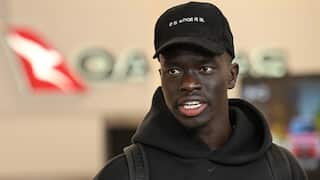 A man in a black cap speaking to reporters