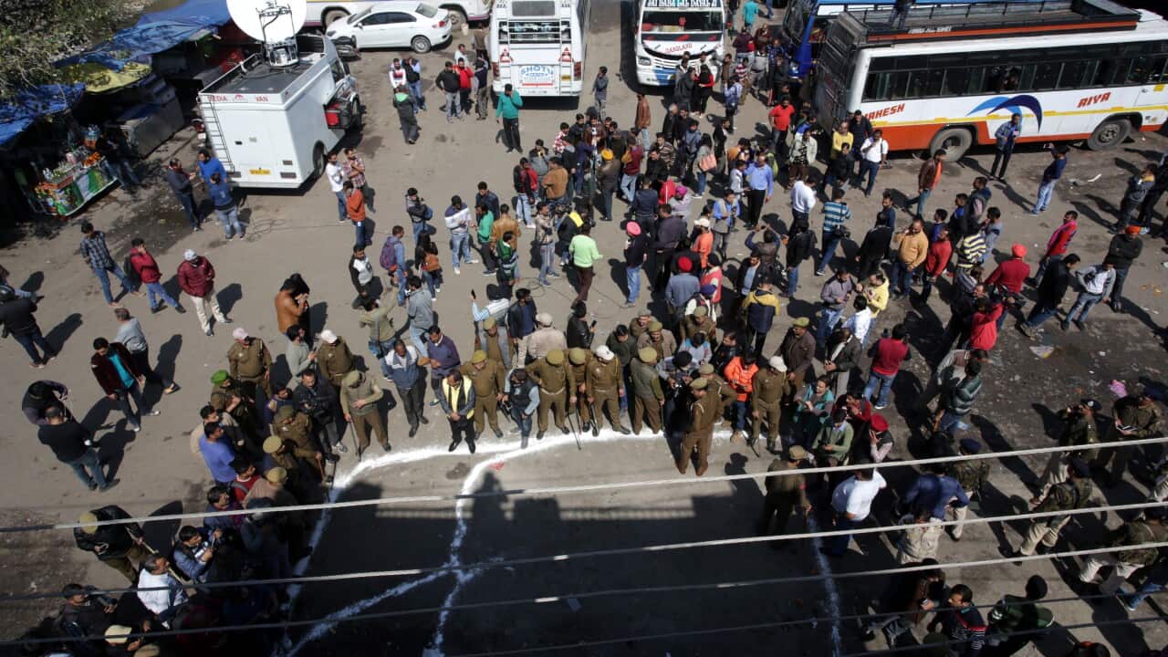 Indian people gather as Jammu and Kashmir police officers stand guard near a grenade blast site, at a general bus stand in Jammu.