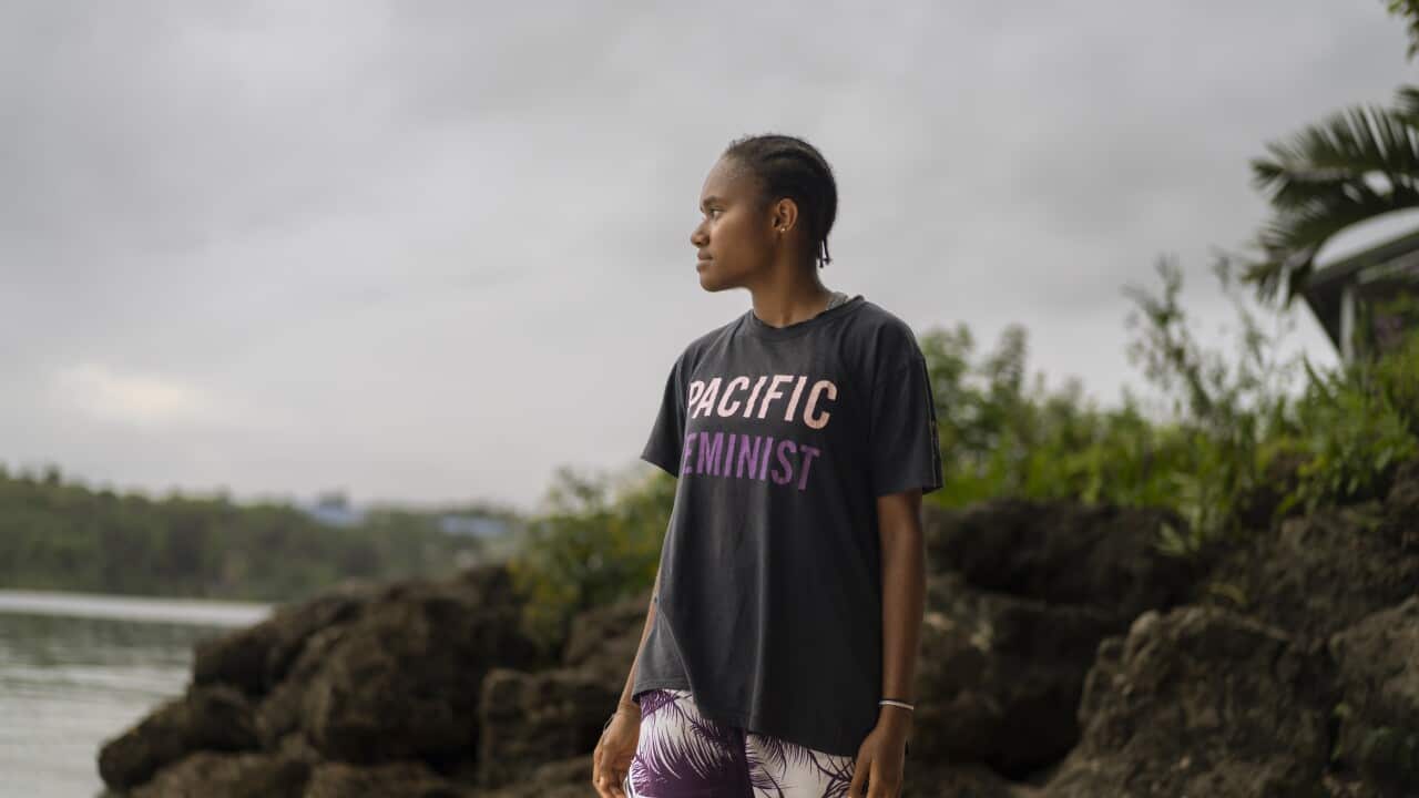 A young woman stands on a coastline, looking out to the ocean