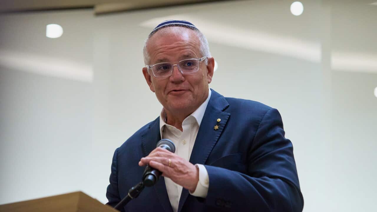 A man wearing a suit and yarmulke holding a microphone at a lectern