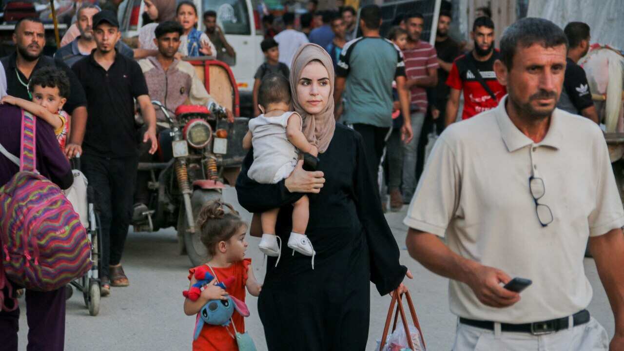 A woman holds a baby, and her belongings as she flees her home.