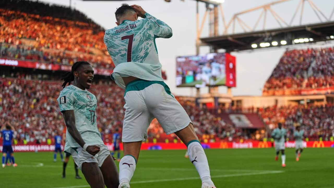 Portugese footballer Cristiano Ronaldo performs his famous "Sui" goal celebration, legs wide, arms crossed over his face as he leaps into the air.