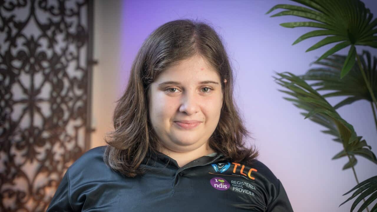 Rita Nichola in a blue t-shirt sitting on a chair in an office.