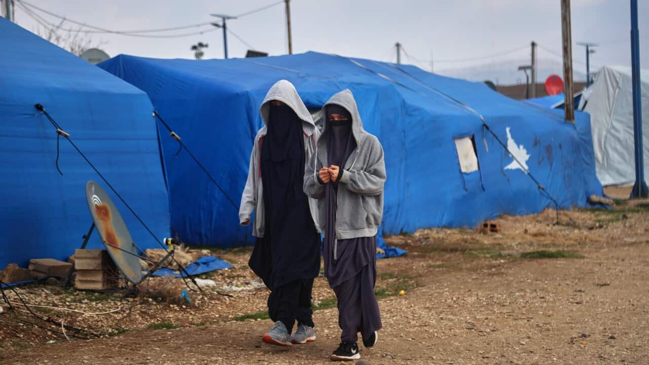 Two women with covered faces walk among tents