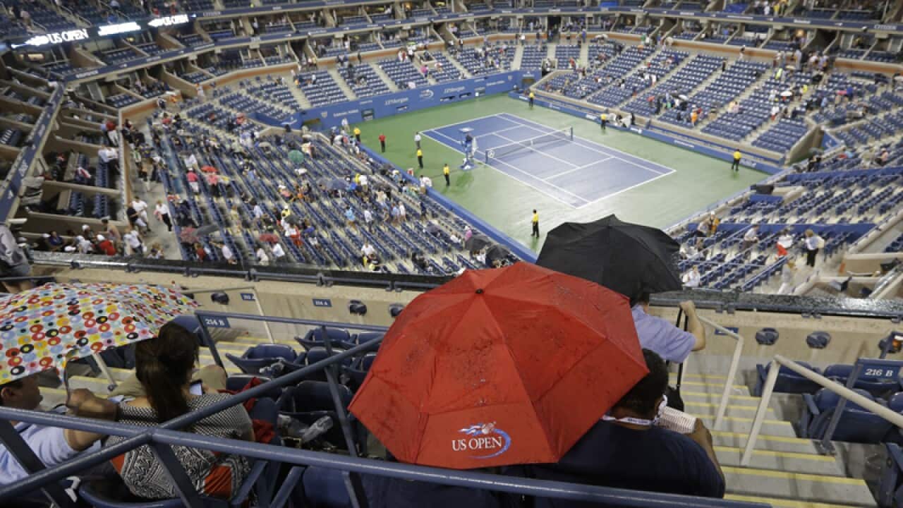 Patrons huddle under an umbrella during a rain delay at the US Open