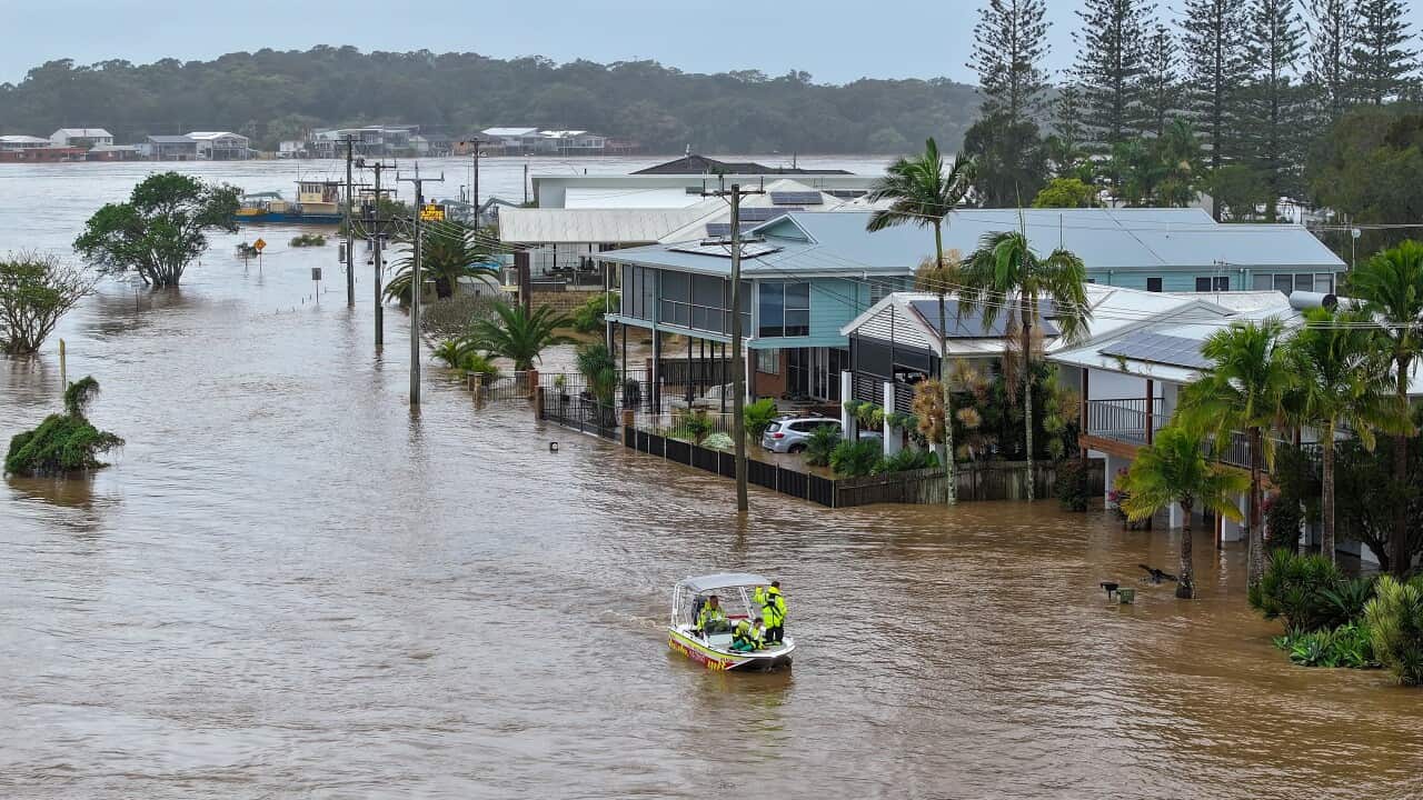 A rescue boat is in the middle of a residential area submerged in brown floodwater.
