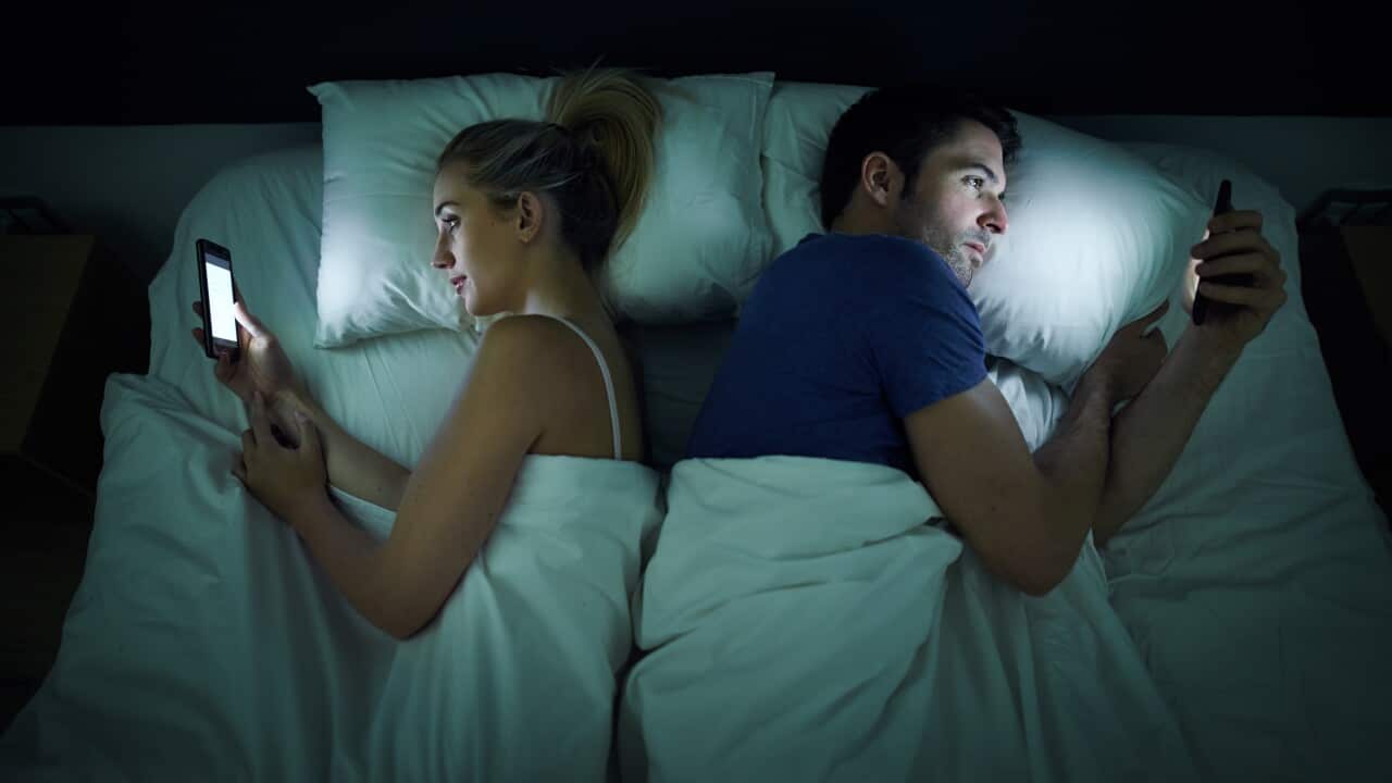 Shot of a young couple using their cellphones in bed at night back to back