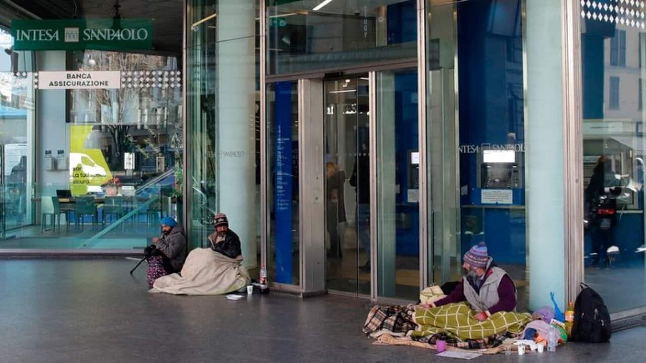 Three homeless sit covering themselves with blankets outside a bank, in Milan, Italy, Friday, Jan. 25, 2019. (AP Photo/Luca Bruno)
