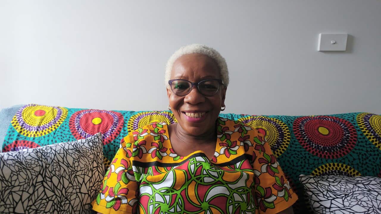 Joy sits on couch smilin at camera with vibrant kenyan print cushions