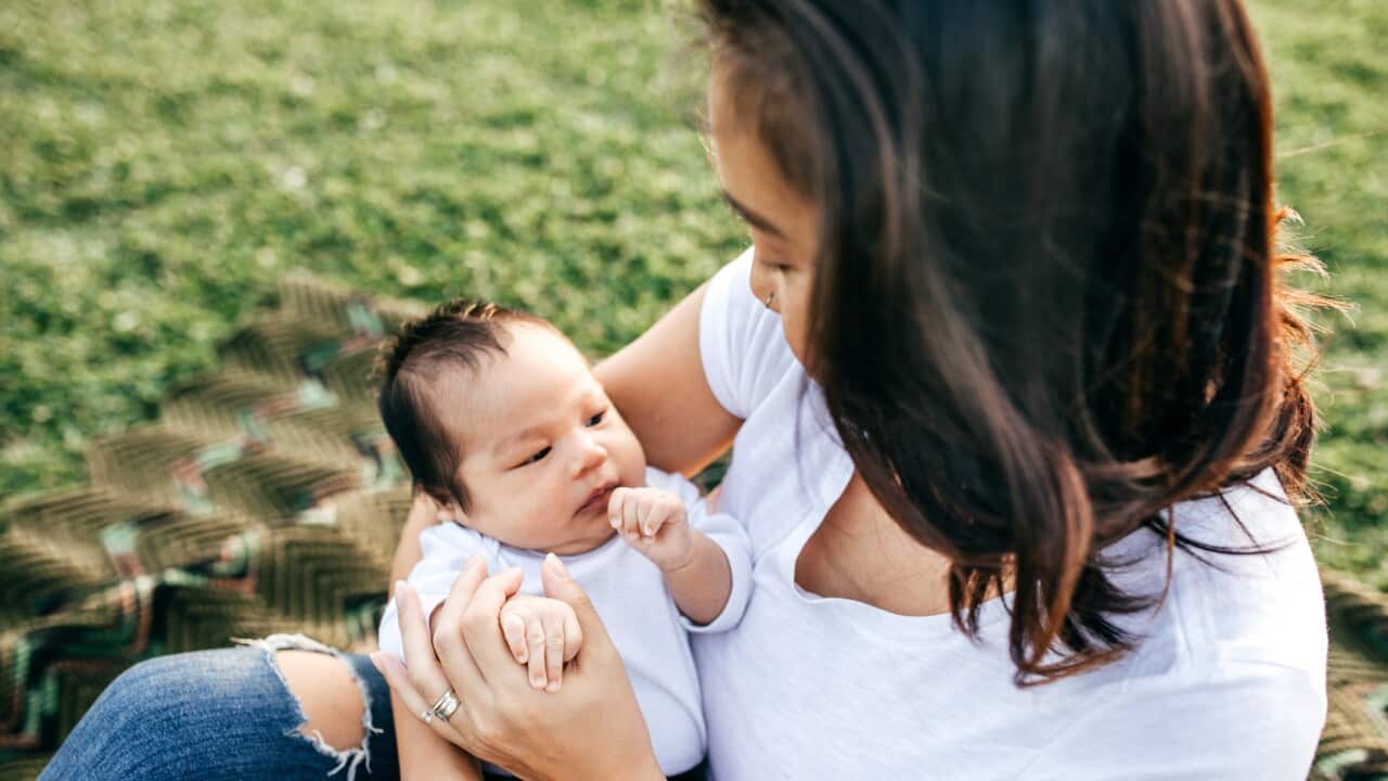 Baby being held by mother on a picnic blanket spread on the grass.