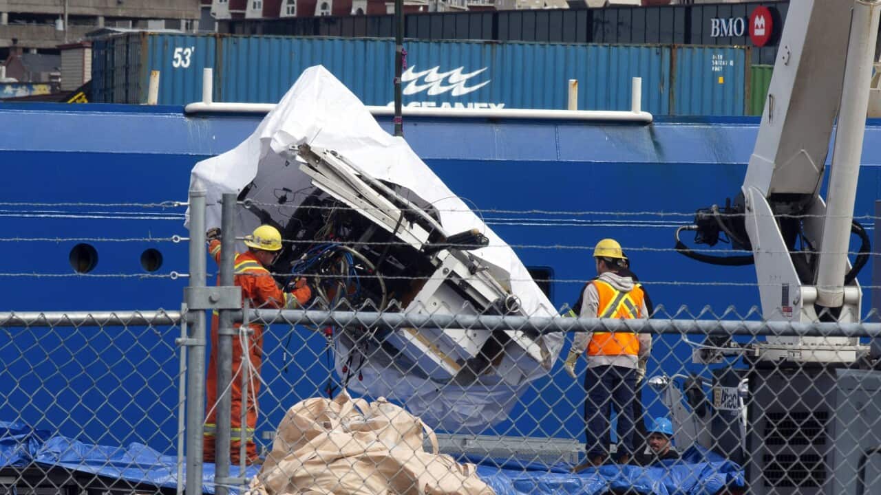 Workers look at a large white object, a wreckage that has been covered by a sheet